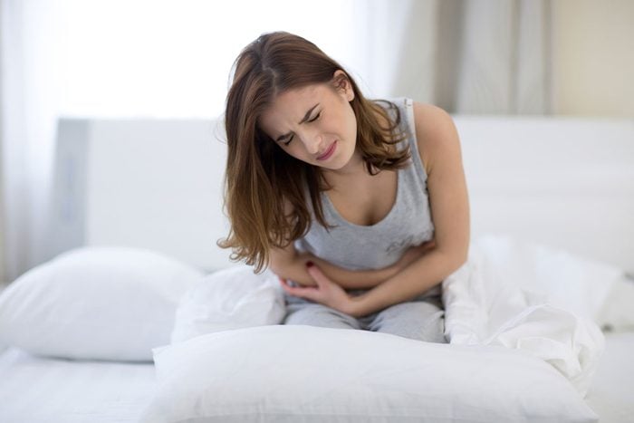 Lactose intolerant woman sits doubled over on her bed