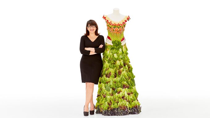 Designer Izzy Camilleri standing with a dress made out of greens