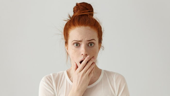 A red-headed woman holds her mouth in shock