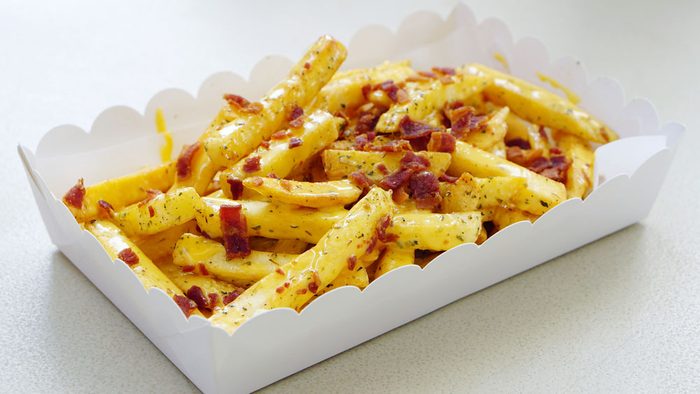 Greasy cheese fries covered in salt and bacon, presented in a pretty scalloped takeout box