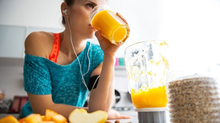 eat for running, a fit woman in her kitchen drinking a peach smoothie