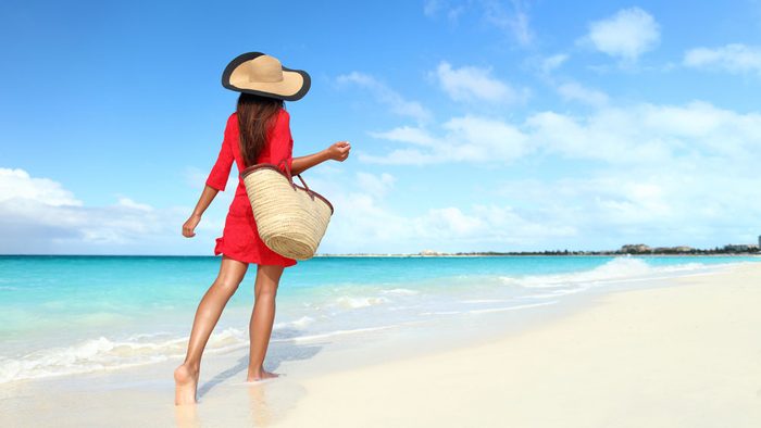 summer layering, a woman walks along the beach with a sun hat, a coverup dress and an oversized tote