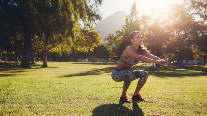 staying motivated in summer outdoor workout, woman doing squats in the park
