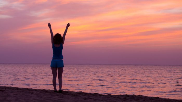 wellness getaways feel good, woman on a beach at sunrise, loving life