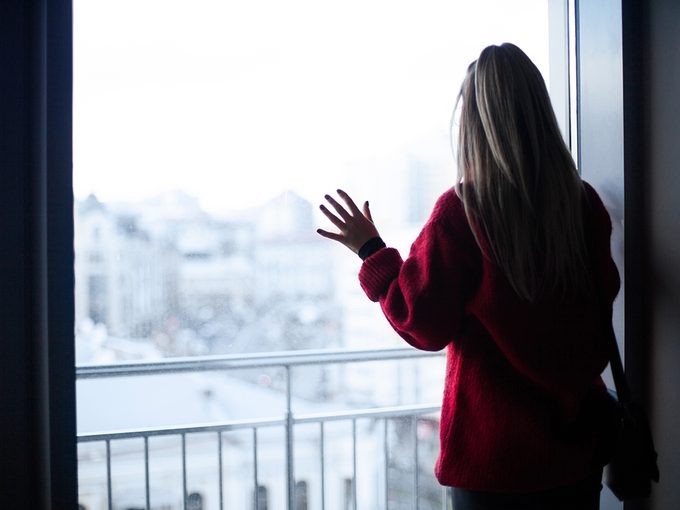 winter depression, a woman in her apartment looks out her window