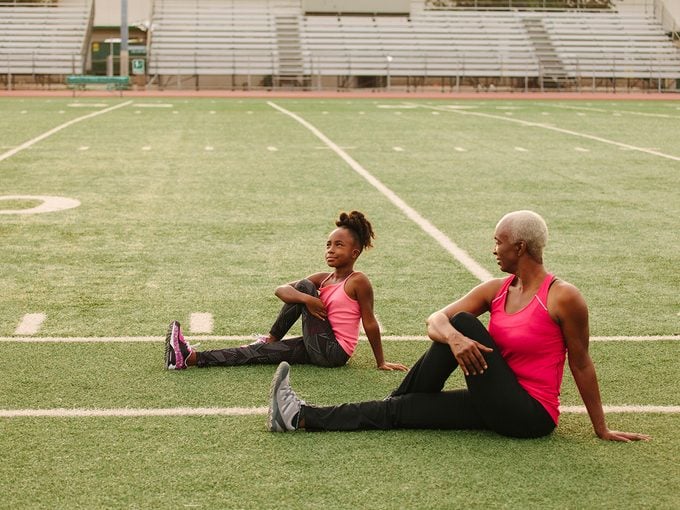 Older woman stretches on field with granddaughter