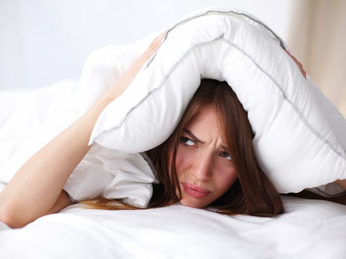Aging, woman in bed frowning with pillow, trouble sleeping
