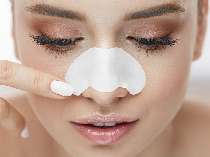 Blackheads, woman about to remove a pore strip from her nose