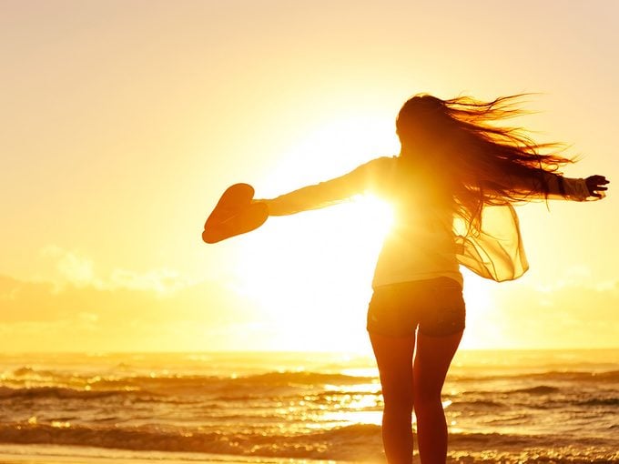 Body image, Woman standing on a beach, silhouetted in front of a sunset, with her arms flung wide