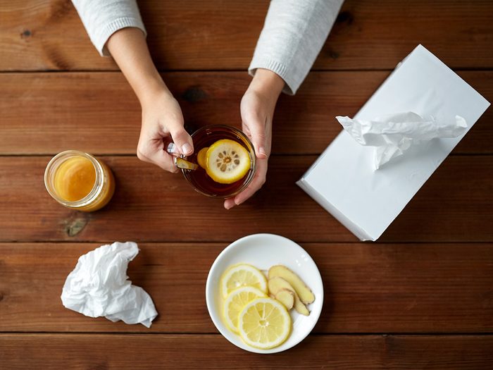 Cold weather, overhead shot of woman drinking lemon tea. Balled up tissues are on the table.