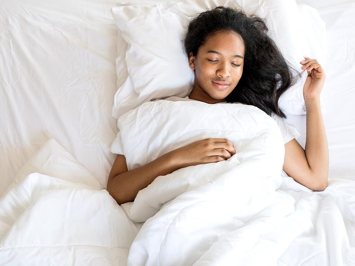 Cold weather, Woman sleeps happily in bed with white sheets and duvet.