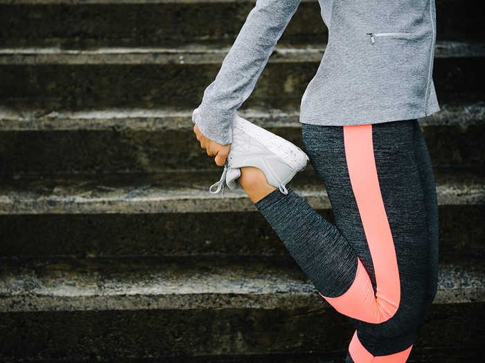 Cold weather, Woman stretching her quads in front of concrete steps. She wears running gear.