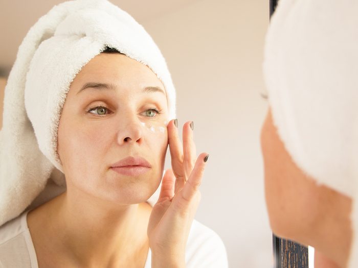 Green tea, woman with hair wrapped in towel applies eye cream