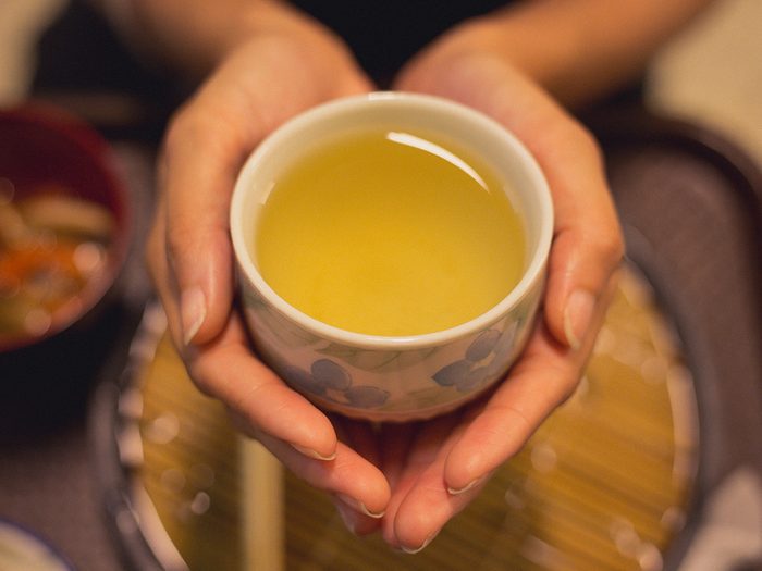 Green tea, Young woman cupping a cup of green tea with no handle. Shot just on her hands.