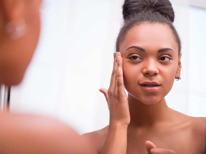 Green tea, young woman checks her skin for acne in a mirror