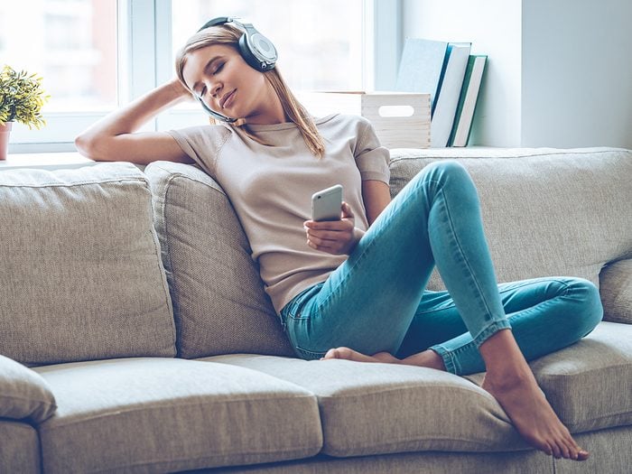 Happiness, woman sitting on couch listening to melancholy music with headphones