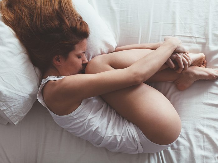 Health myth, A woman lies curled up in bed with a sad look on her face due to sexual pain