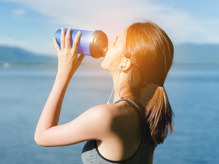 Healthy eating, Woman just finishes her workout and stands by a lake guzzling water from her water bottle.