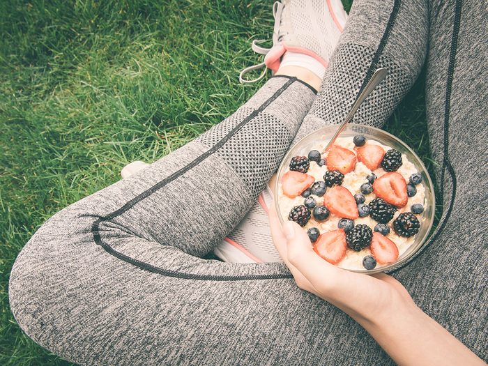 Healthy eating, Woman sits in workout clothes in grass and eats oatmeal and fruit