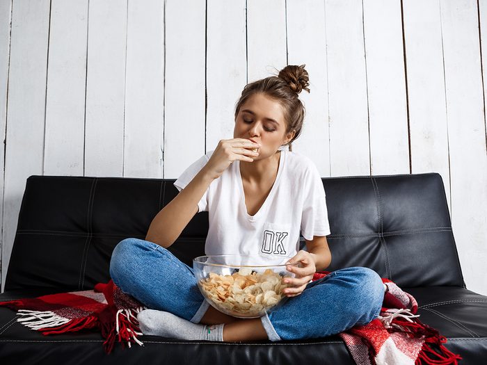 Healthy eating, woman sitting on the couch stuffing her face with chips