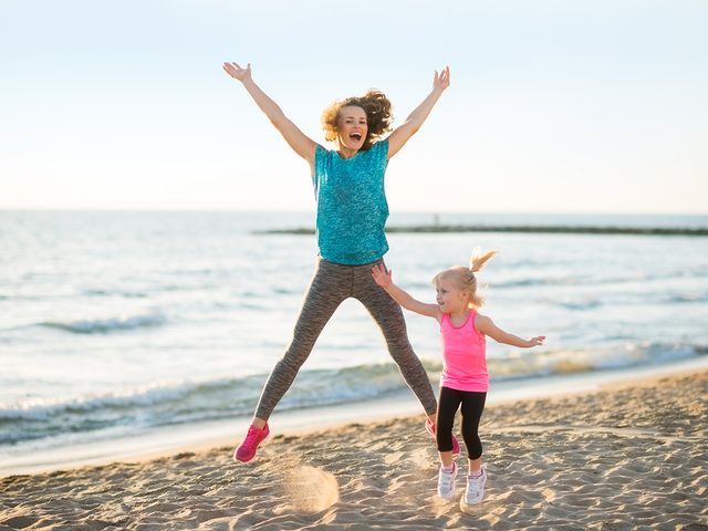 Active mom and daughter jumping on the beach
