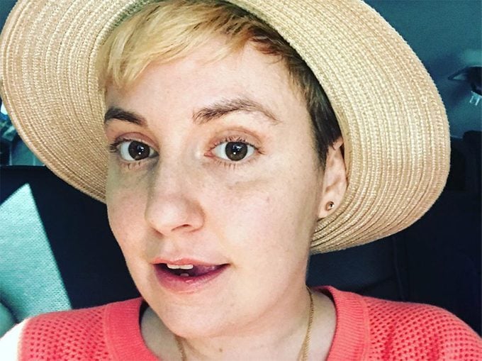 Lena Dunham smiling in hat. She just had a hysterectomy.