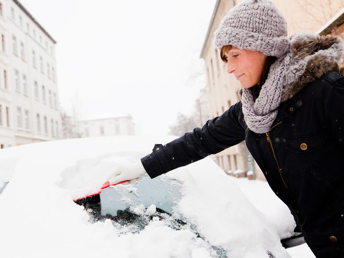 Rainy mood, woman scraping snow off a car