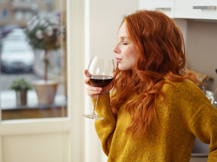 Redhead woman sniffing glass of wine in kitchen