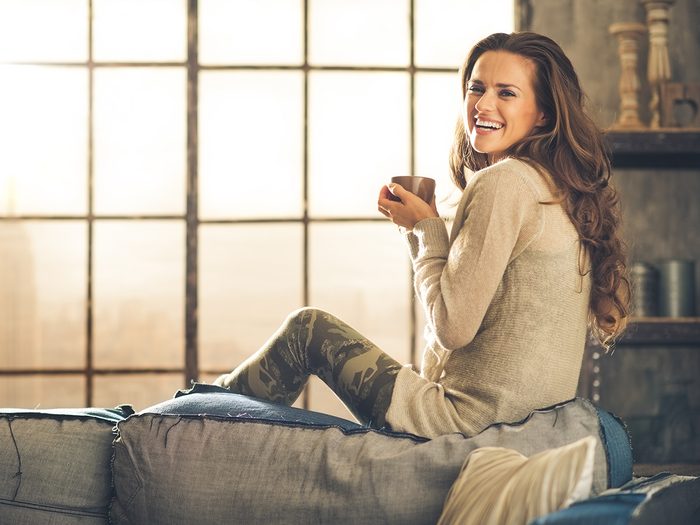 Happiness, woman sitting on couch with cup off coffee and smling