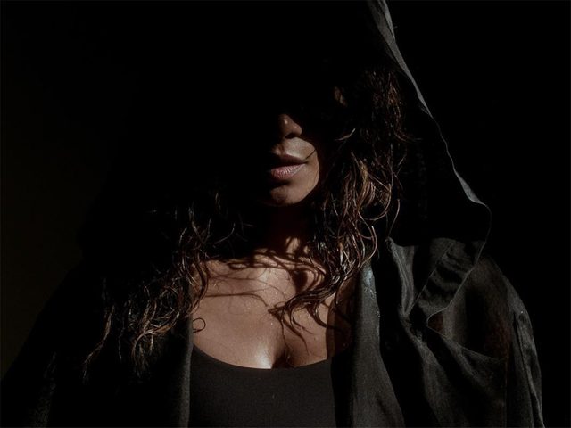 Halle Berry stands in shadow with a boxing robe hood partially covering her face