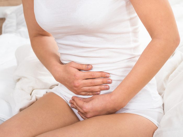 Health snack, woman clutching her stomach as she sits on the edge of the bed because she has constipation