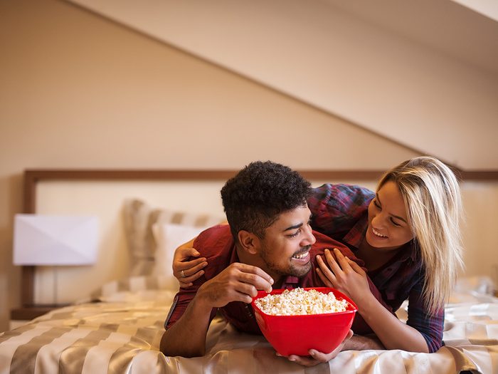 Healthy snacks, couple lying on bed eating popcorn