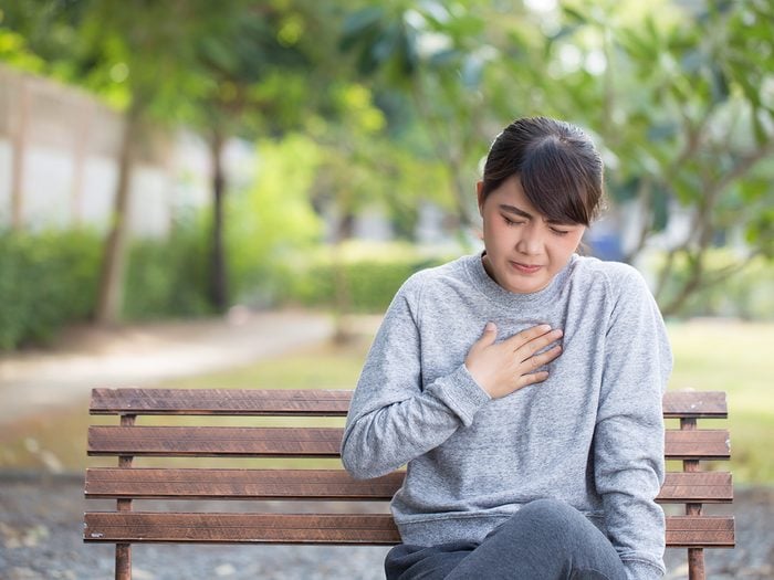 Woman with heartburn clutching her chest on a park bench outside
