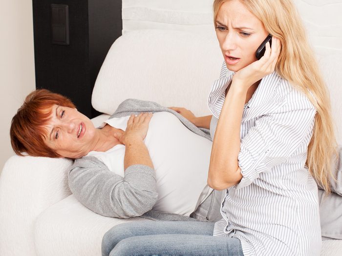 A woman lies on a couch clutching her chest while another woman calls 911, heartburn or heart attack?