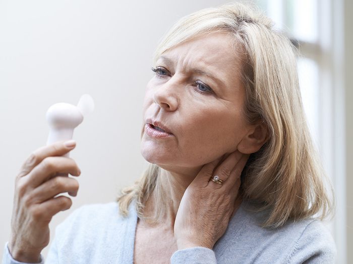 Menopause symptoms, sweating middle-aged woman fans herself with small electric fan