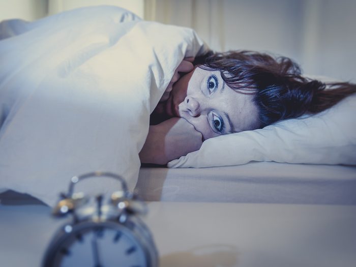 Menopause symptoms, woman lies in bed wide awake and stares at alarm clock because she can't sleep