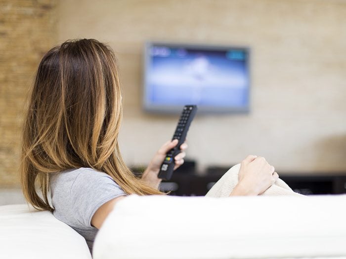 Self love, woman holds up remote control as she watches TV on the couch