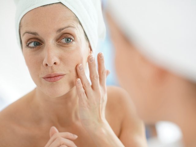 Skin care routine, Mature woman applies face cream in the bathroom