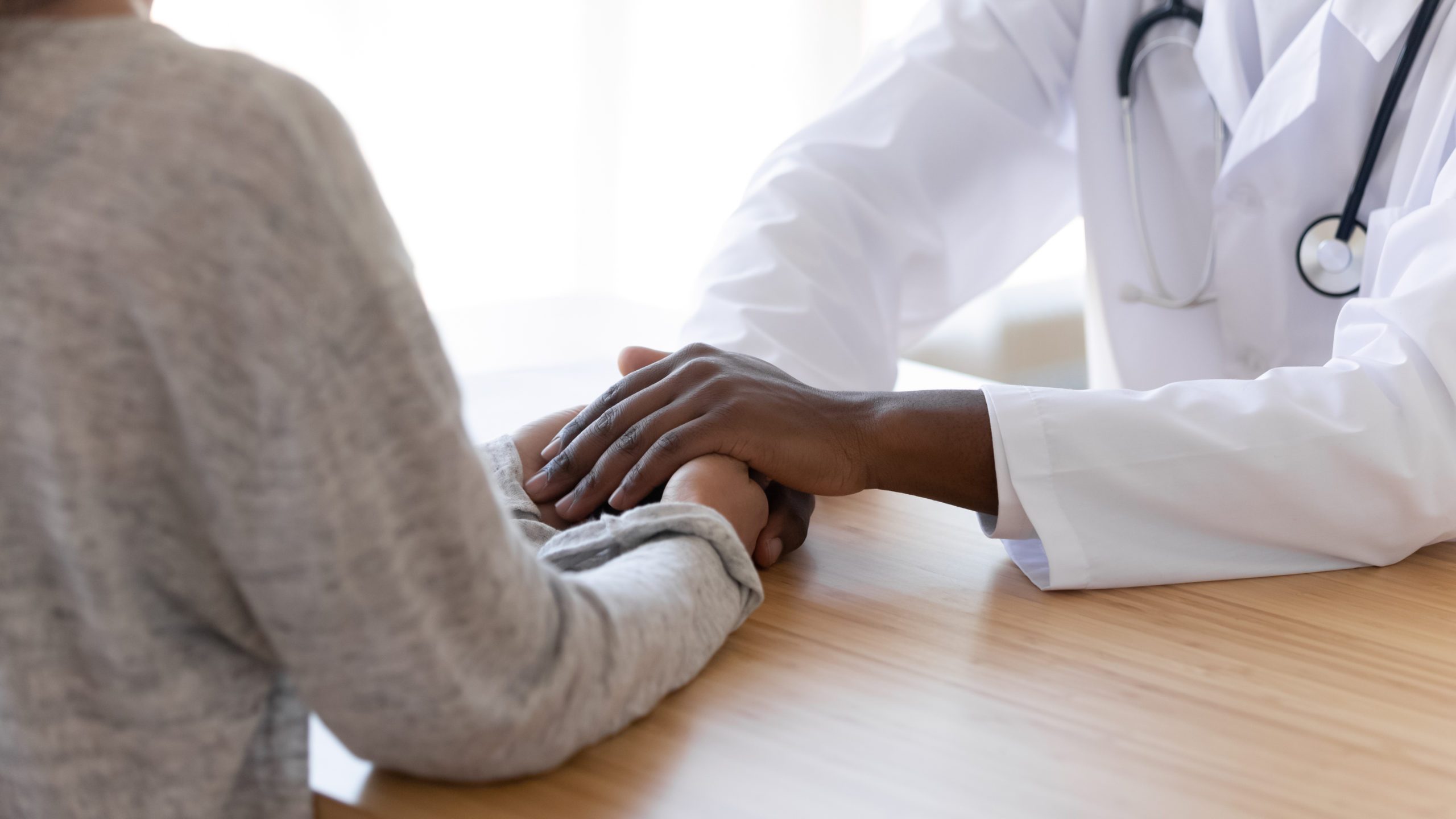 Black,male,doctor,holding,hands,of,female,patient,at,meeting