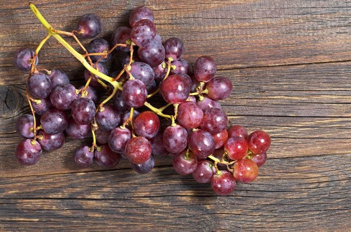 Red grapes on old wooden table, top view