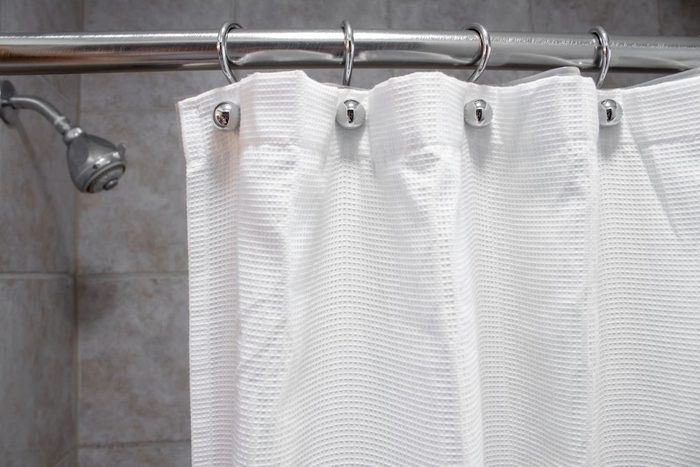 a white shower curtain in an empty shower with water ON medium shot