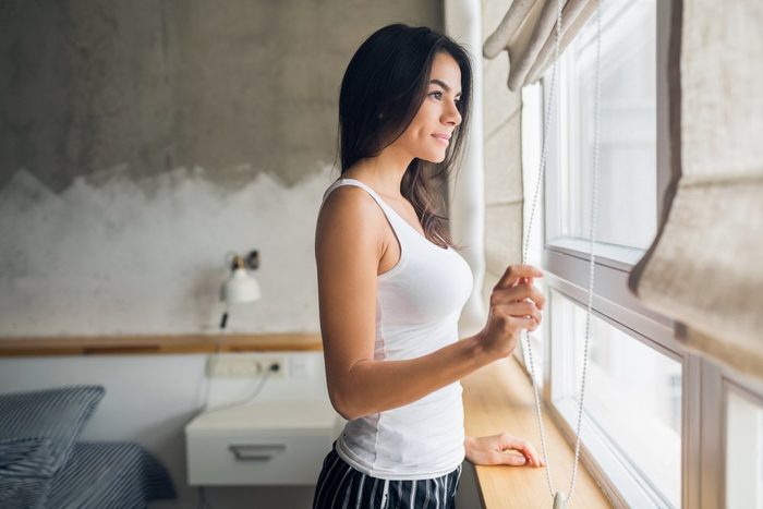 young attractive brunette woman in bedroom opening curtain, looking in window, morning time, smiling, lifestyle, natural beauty, feeling comfortable at home