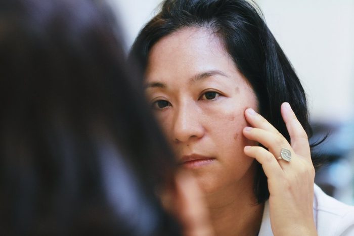 40s Asian woman looking on her face skin in the mirror and look worried or concern about the Aging skin problem.Brownish colored patches or melasma appear on the cheeks.