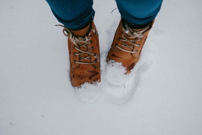 Vintage pair of yellow working and trekking boots, stepping on snow-covered surface.