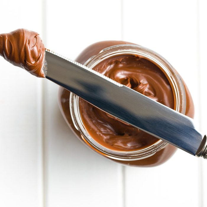 Chocolate spread with knife on white table