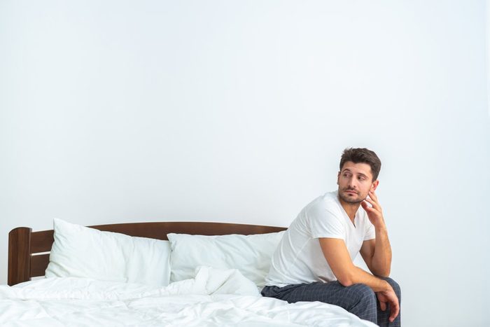 The sad man sitting on the bed on the white background