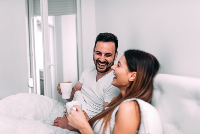 Couple in bed drinking coffee and laughing.