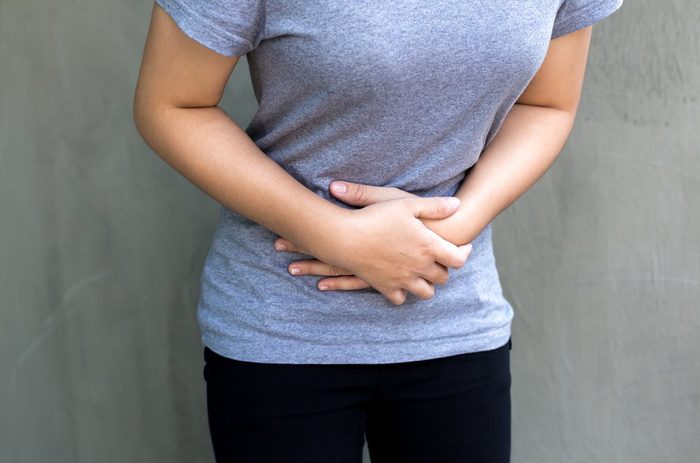 Young woman having a menstruation pain in gray concrete background