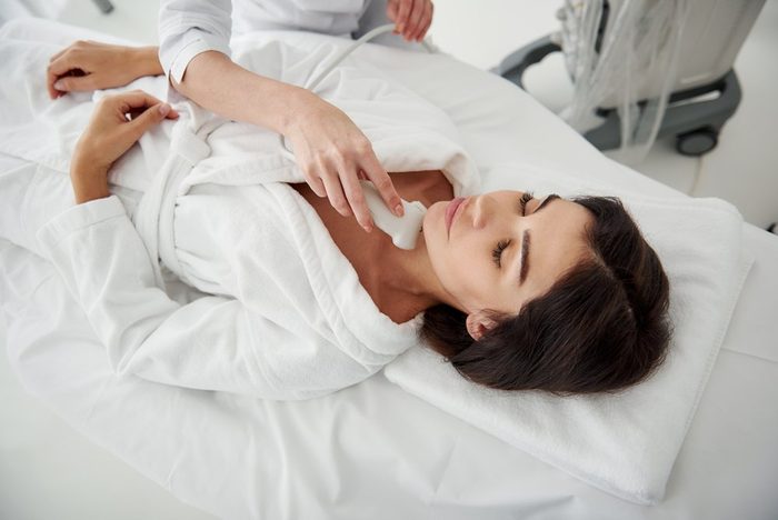 Portrait of beautiful lady in white bathrobe having ultrasound scanning of thyroid