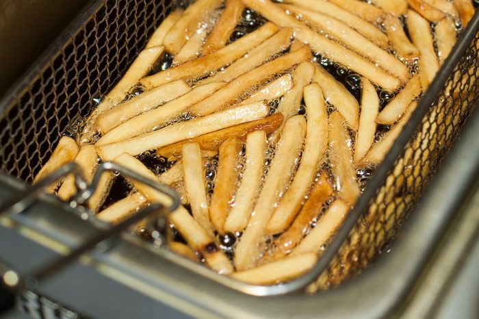 French fries cooking. Grid with strips of potato lowered into boiling oil. The concept of fast food, delicious food, restaurant